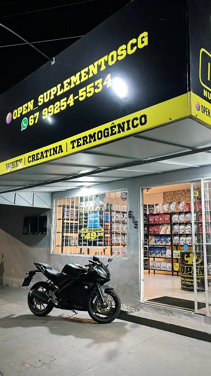 Fachada da Open Suplementos à noite, com o letreiro amarelo aceso